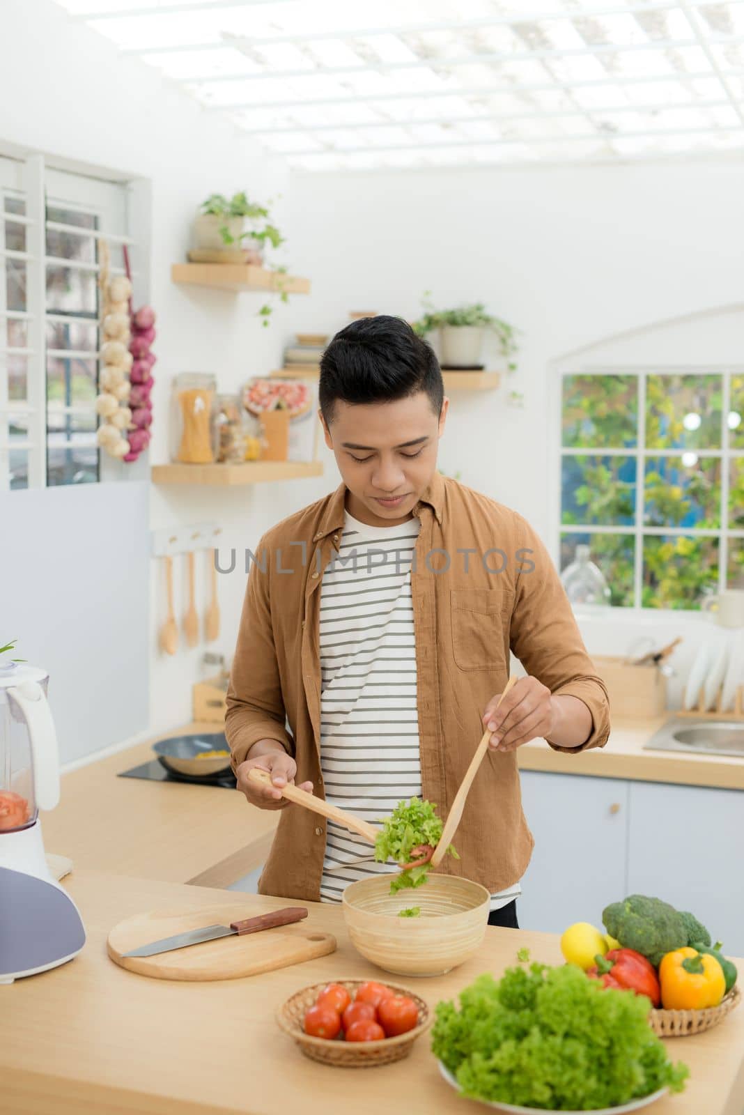 Smiling young man making vegetables salad in the kitchen at home by makidotvn