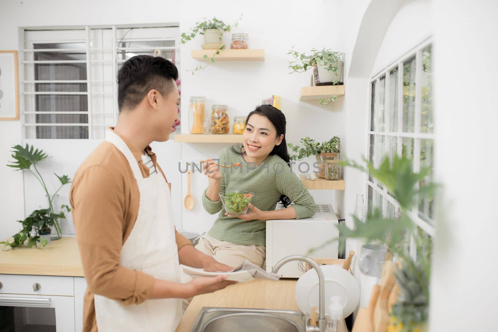 Asian couple eating breakfast early in the morning in the kitchen and having a good time. by makidotvn