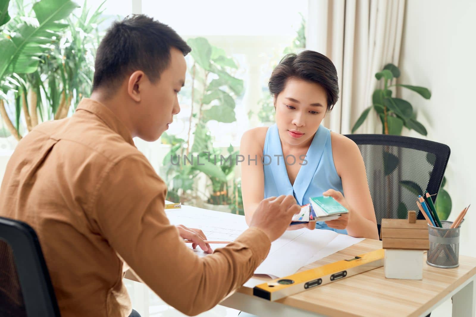 Finding solution together. Confident young man and woman looking at blueprint together while both standing in office by makidotvn