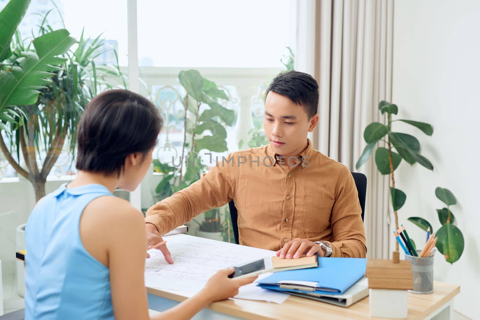 Finding solution together. Confident young man and woman looking at blueprint together while both standing in office by makidotvn