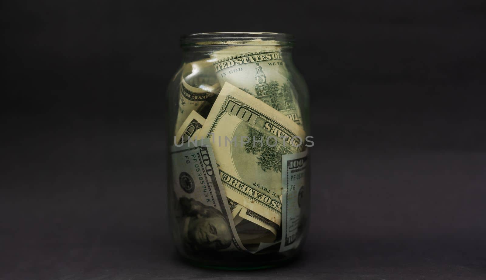 A glass jar full of dollars between one dollar bills. An easy way to save real money.