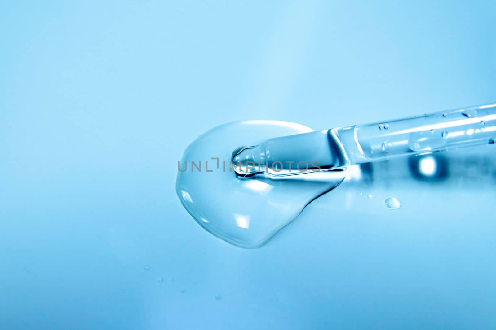 Water bubbles with cosmetic liquid drops of serum on a blue background of a laboratory glass pipette. Close-up of a pipette with drops.