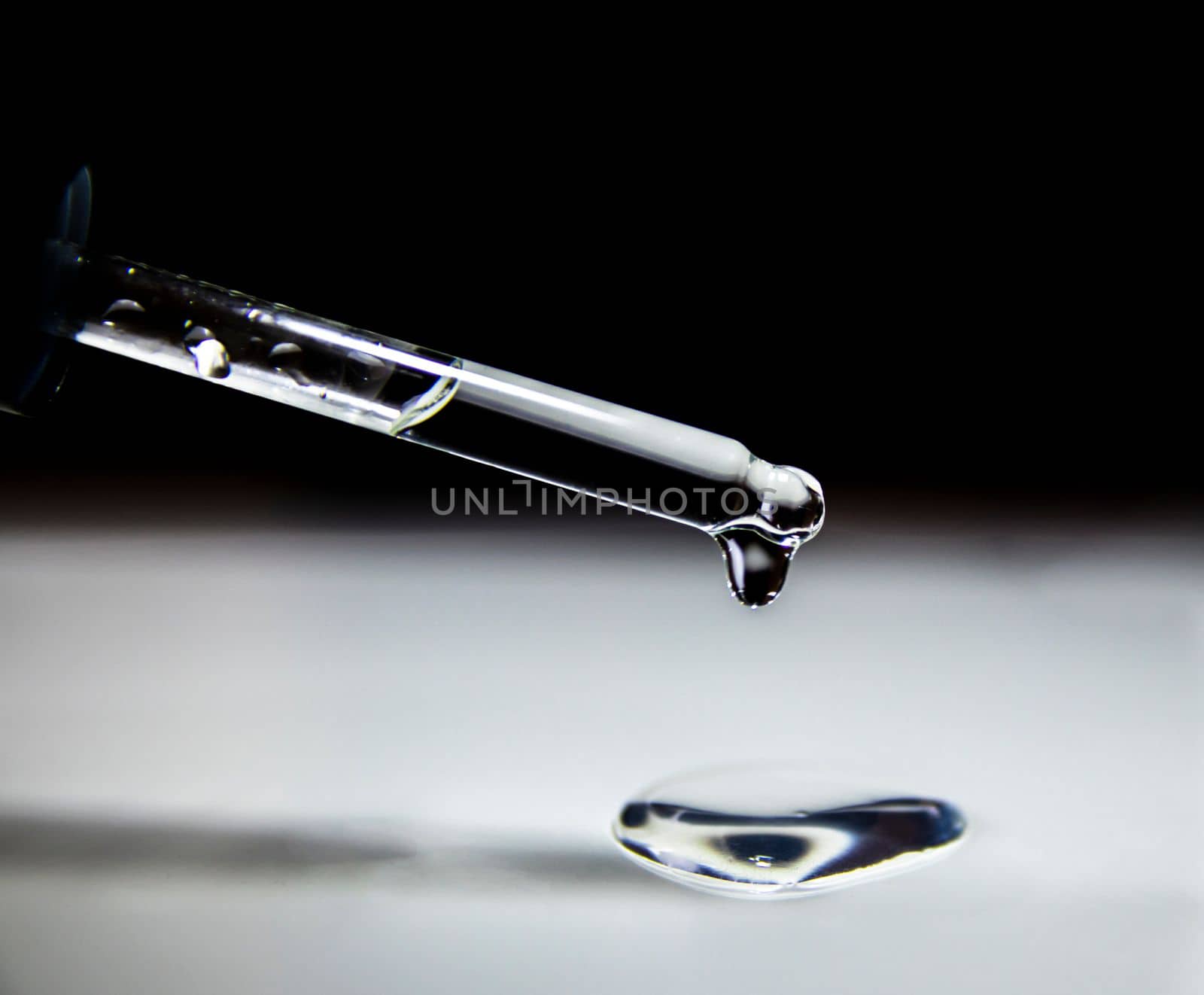 Liquid transparent gel drips from a serum pipette with drops on a light background. Close-up.