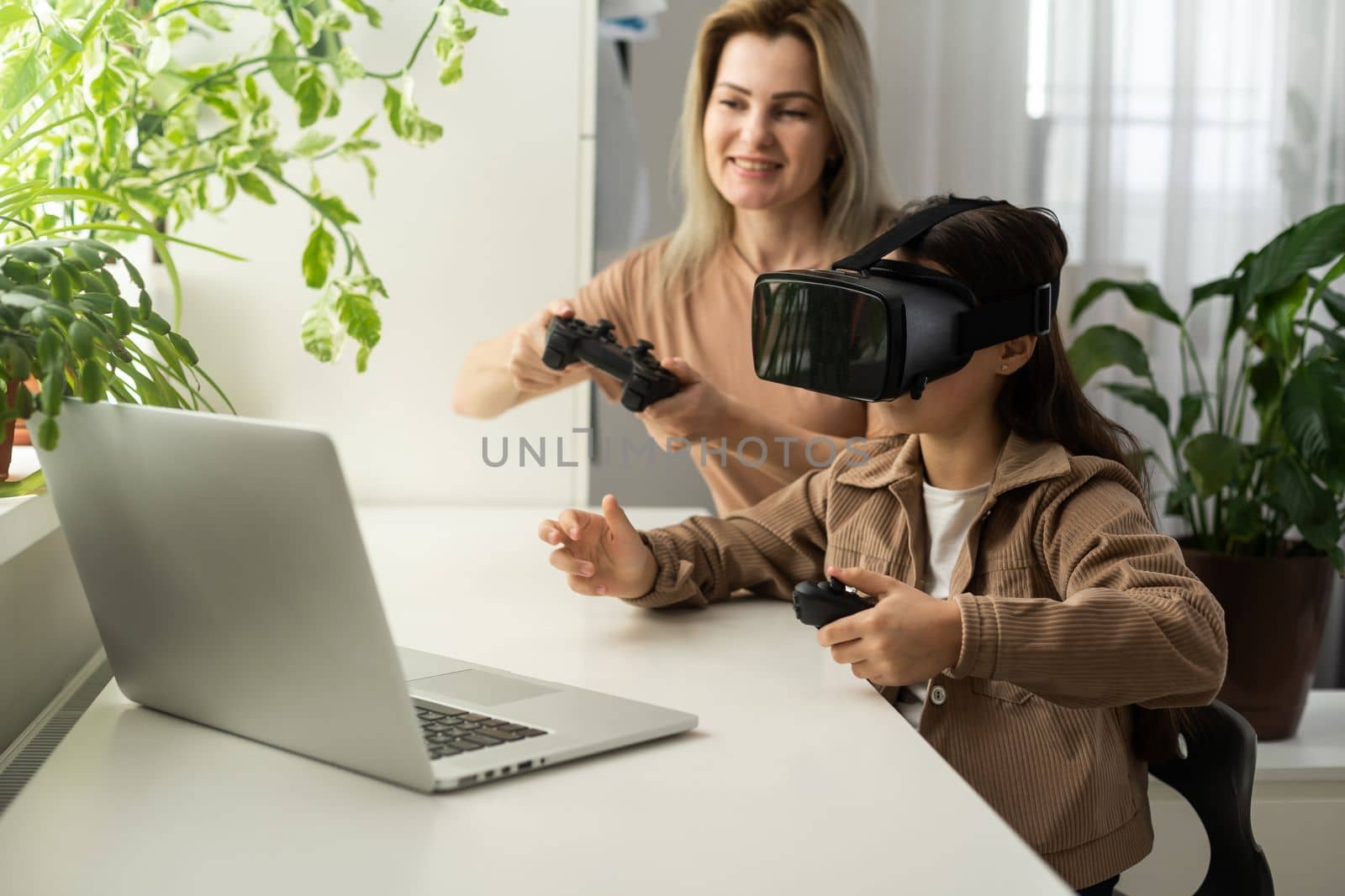 Families and new technologies. Smiling work-at-home mother sitting with daughter wearing vr helmet exploring virtual reality. Curious child teen girl testing AR technology for education.