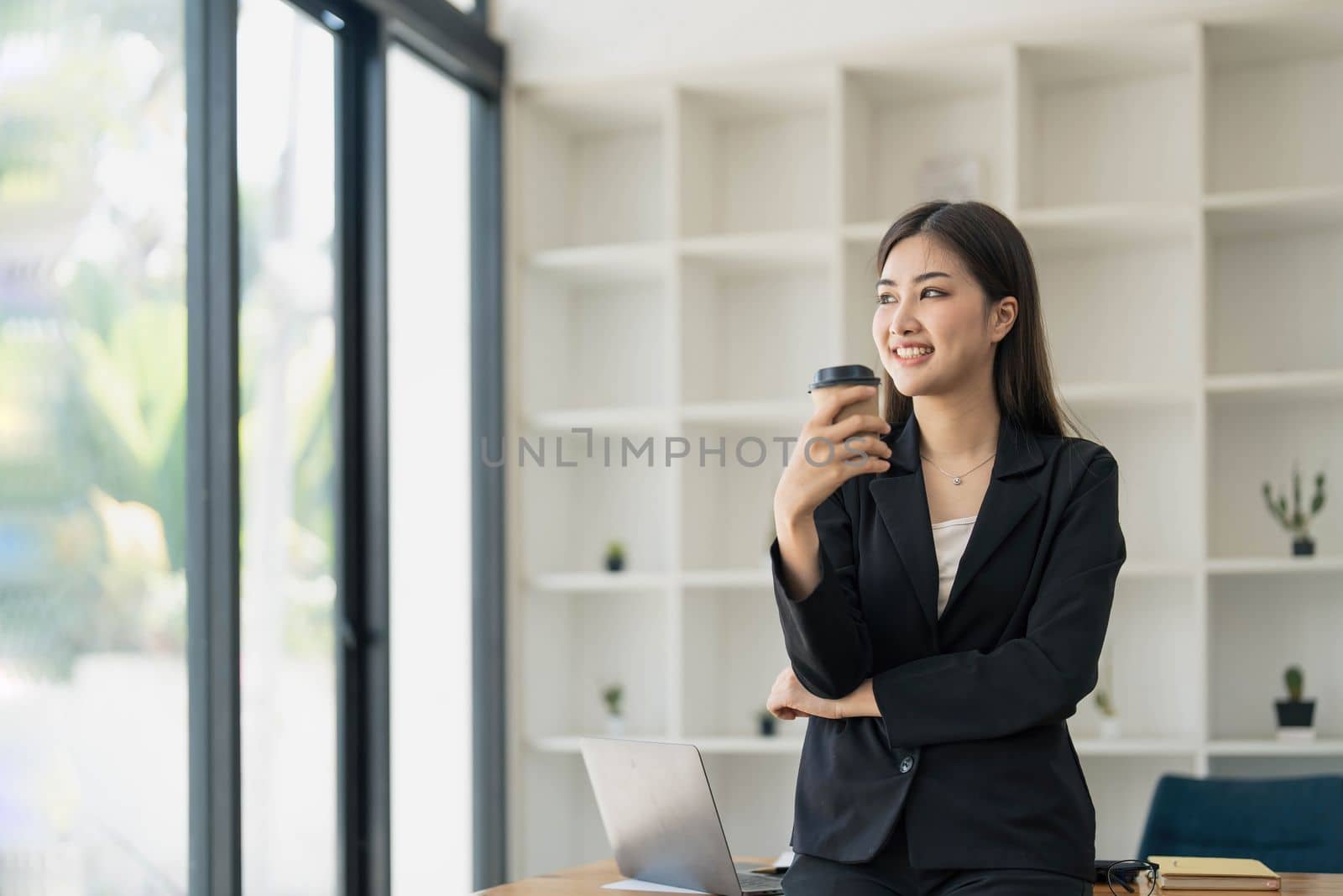 Portrait of young confident woman holding coffee cup, standing at office and looking outside. Successful businesswoman standing in office with copy space. by wichayada