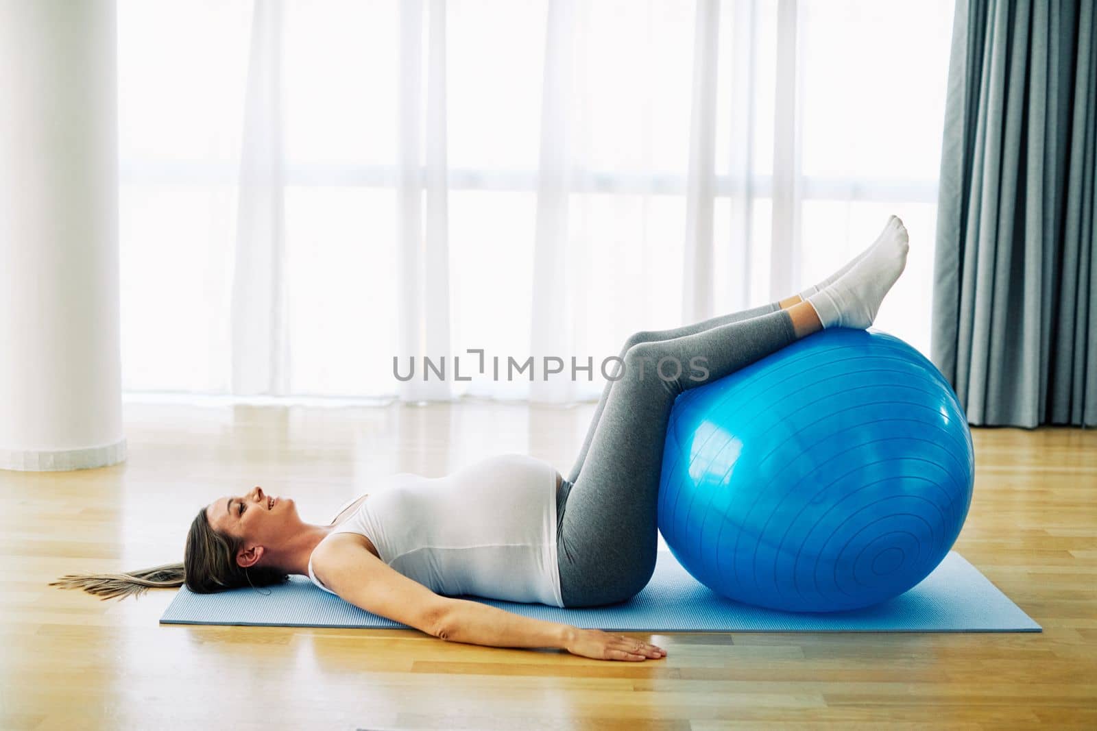Portrait of a young happy pregnant woman doing exercise with a ball at home or in a gym