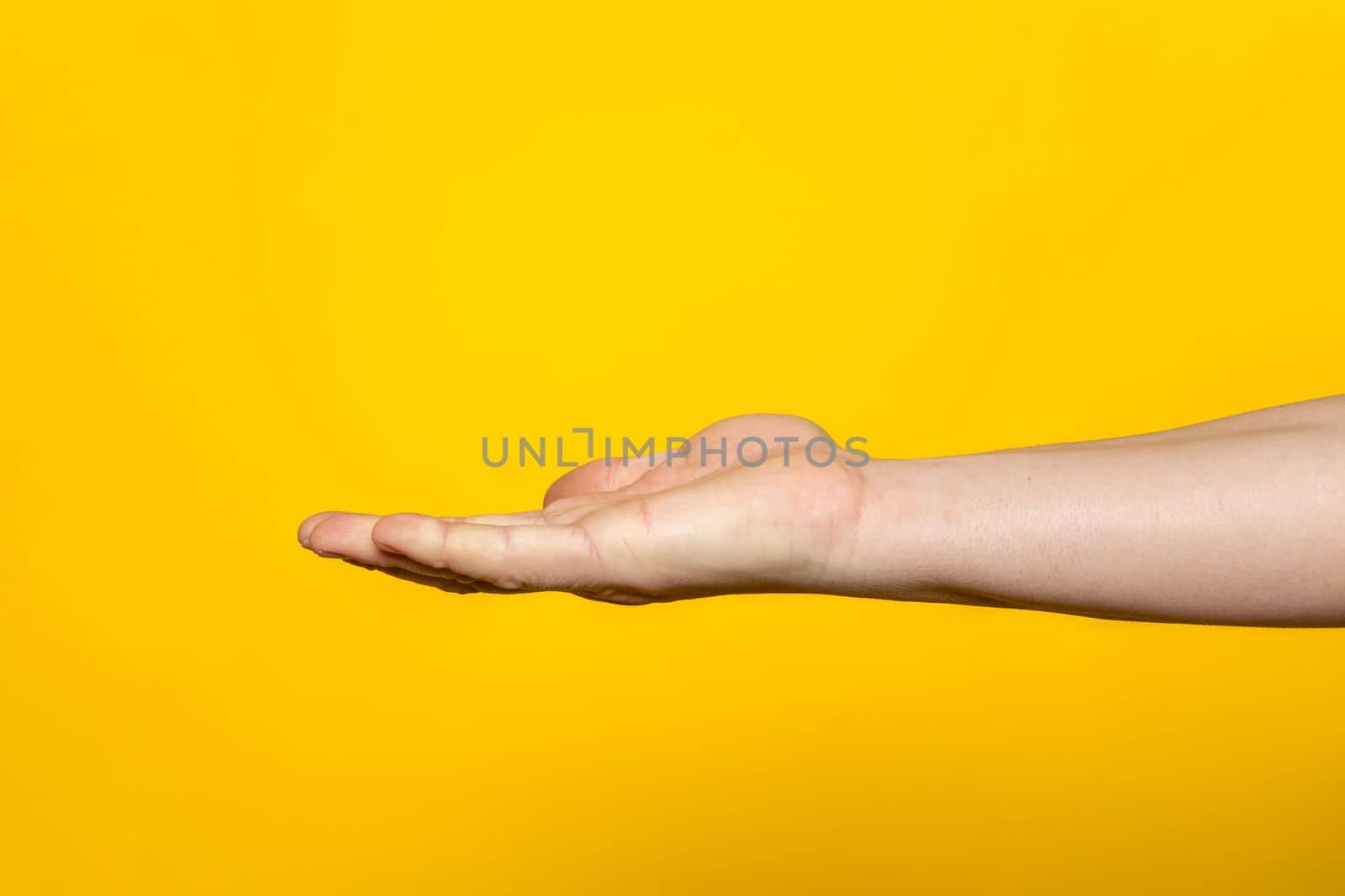 Strong hand of man with palm up presenting an imaginary product in advertising concept isolated on yellow background