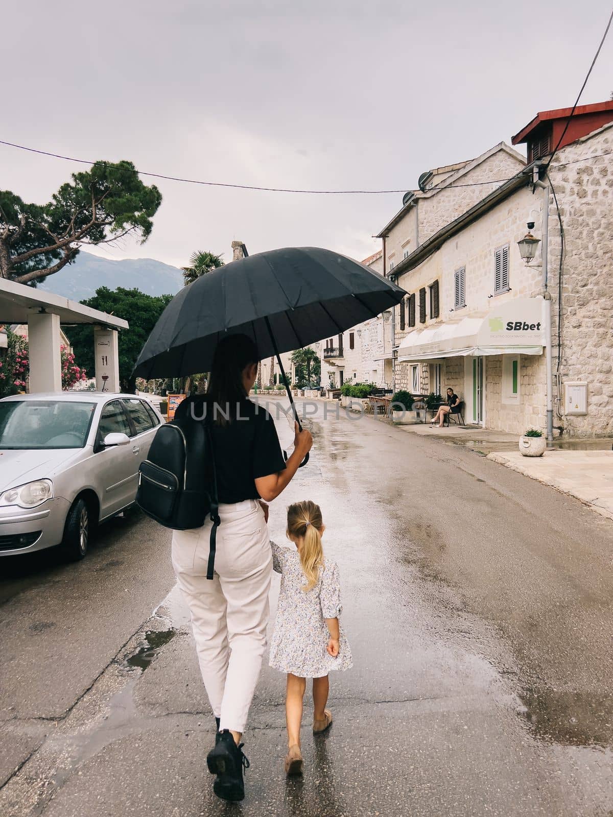 Mom and a little girl are walking down the street under an umbrella holding hands. High quality photo