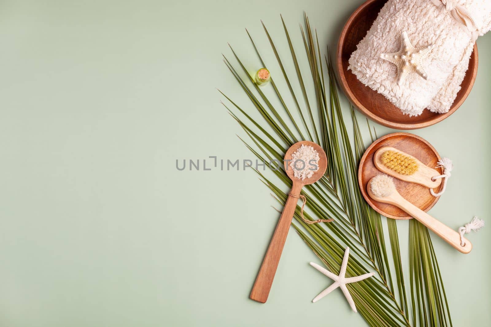 spa composition with palm leaf, towel, sea salt and starfish, light green background, top view