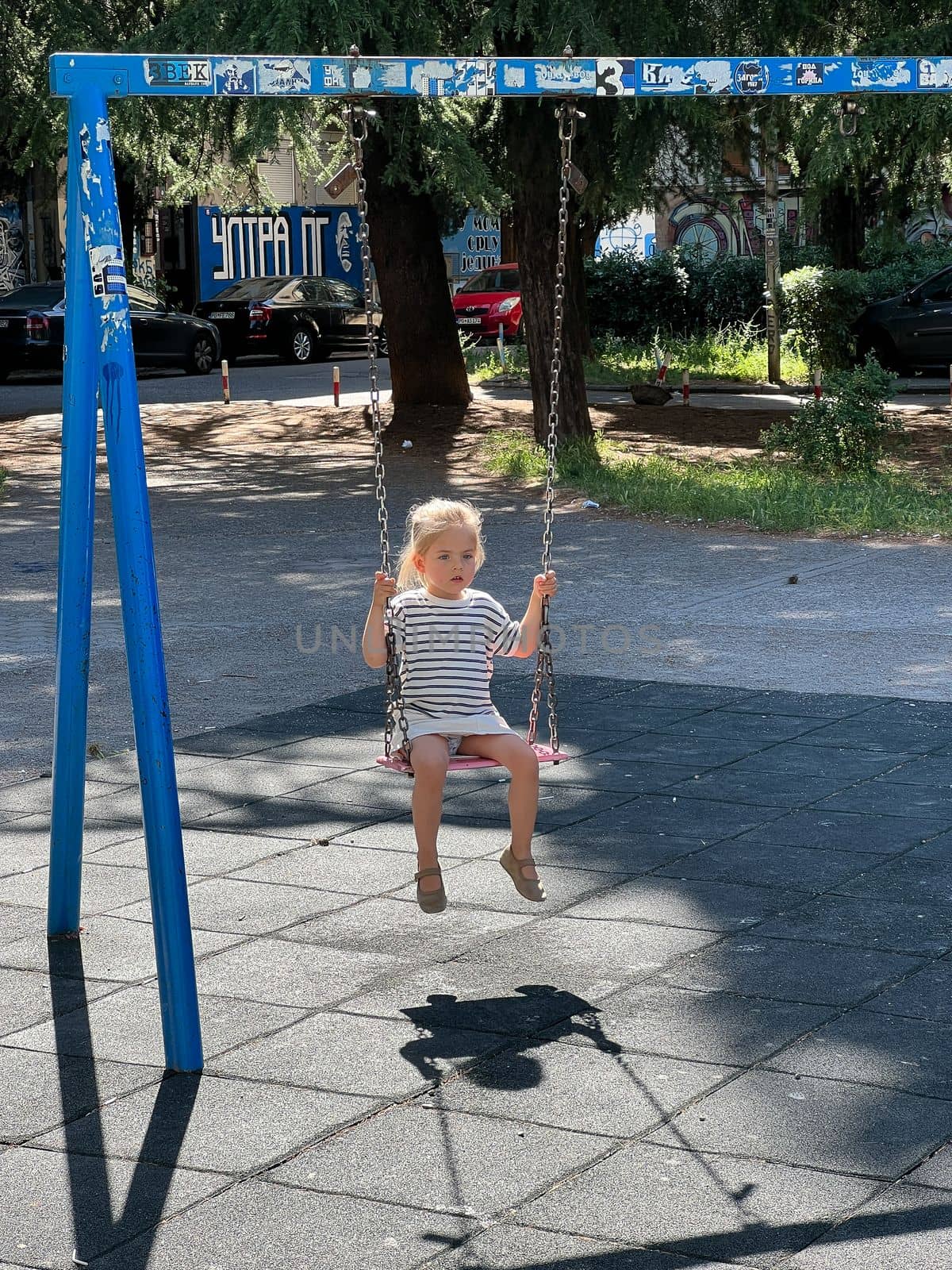 Little girl sits on a chain swing on the playground. High quality photo