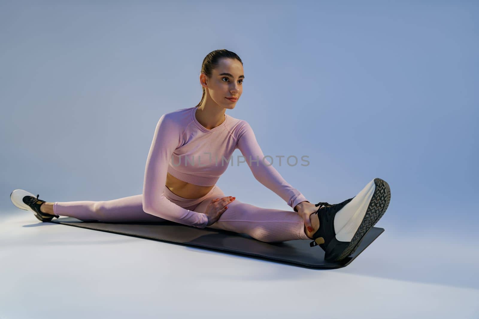 Athletic woman in sportswear doing stretching exercises on yoga mat on studio background