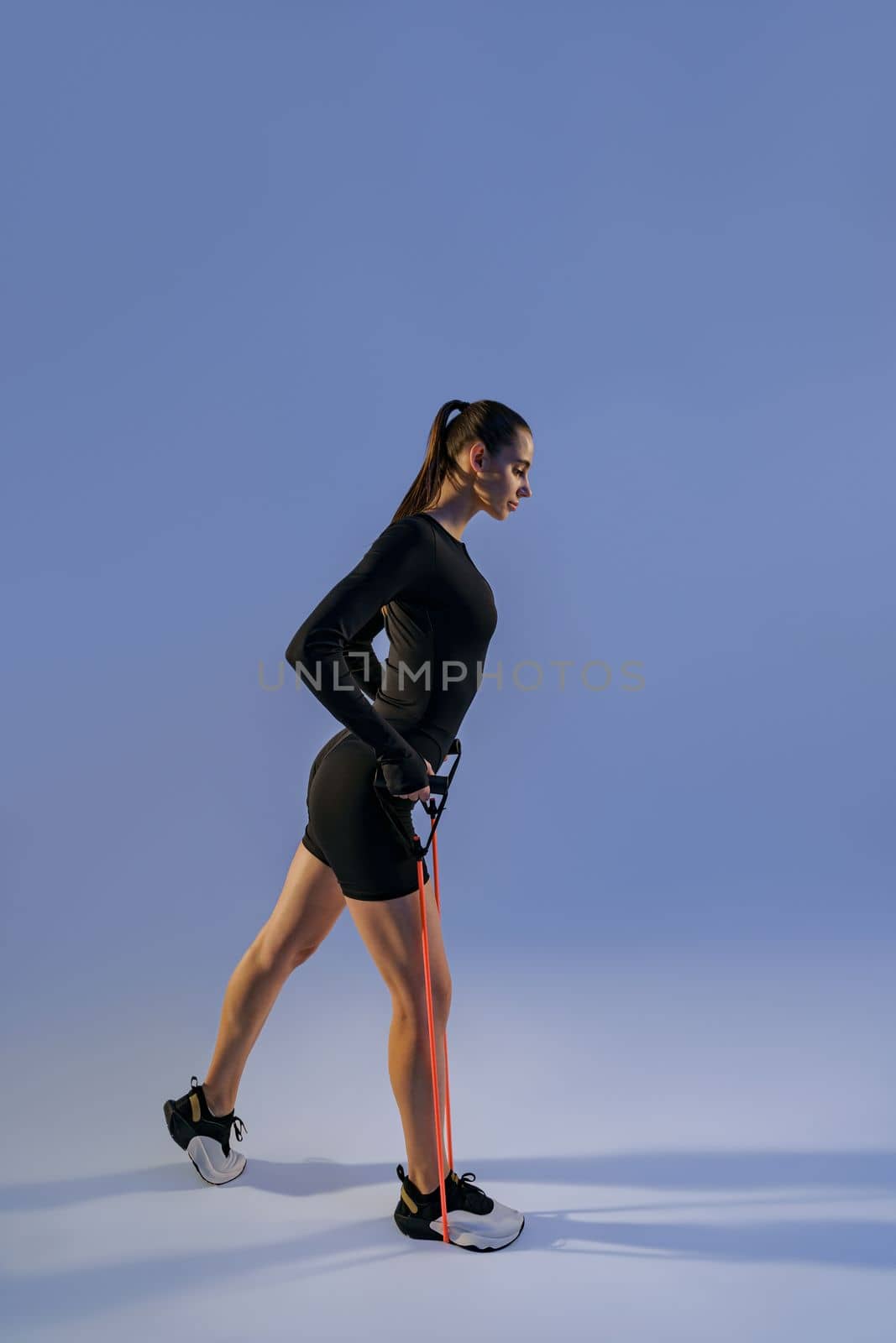 Woman performs exercises with expander on studio background. Strength and motivation