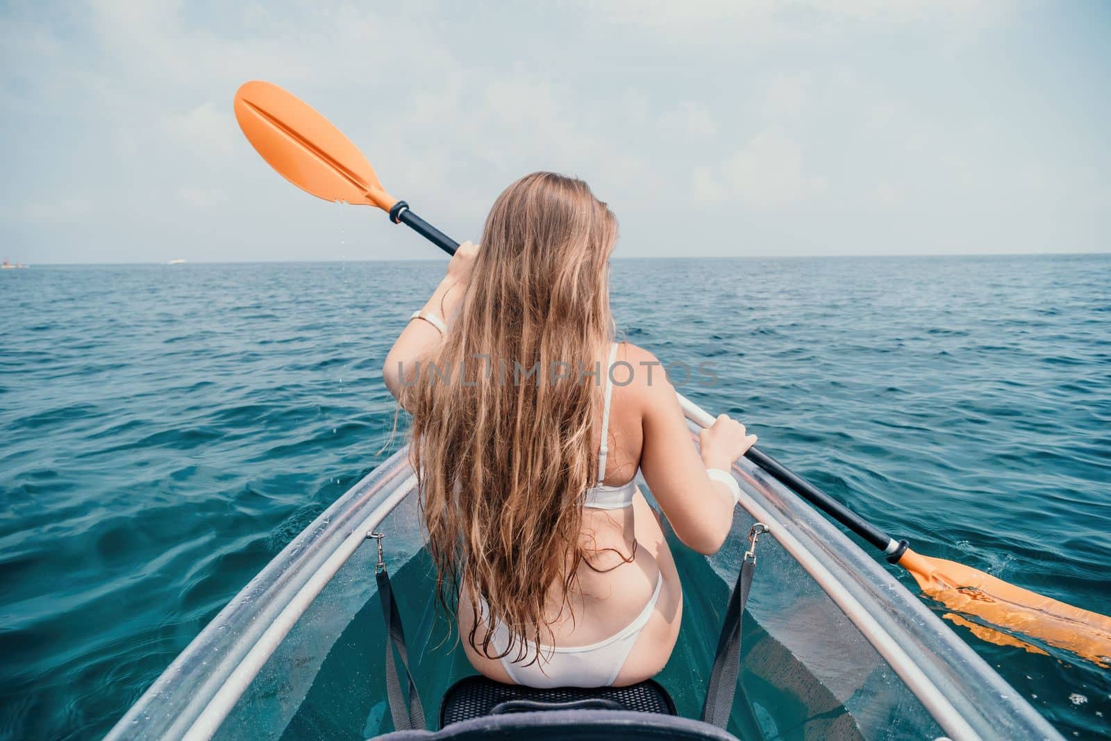 Woman in kayak back view. Happy young woman with long hair floating in transparent kayak on the crystal clear sea. Summer holiday vacation and cheerful female people relaxing having fun on the boat by panophotograph