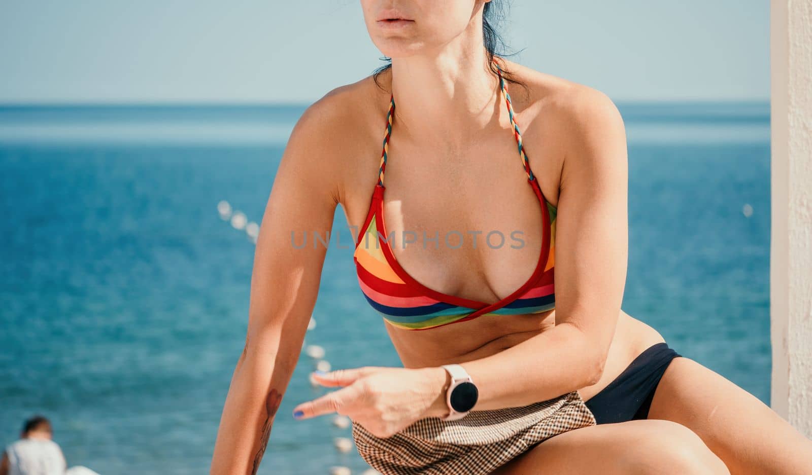 Woman in rainbow bikini. Happy tanned girl in rainbow swimsuit at seaside, blue sea water in background