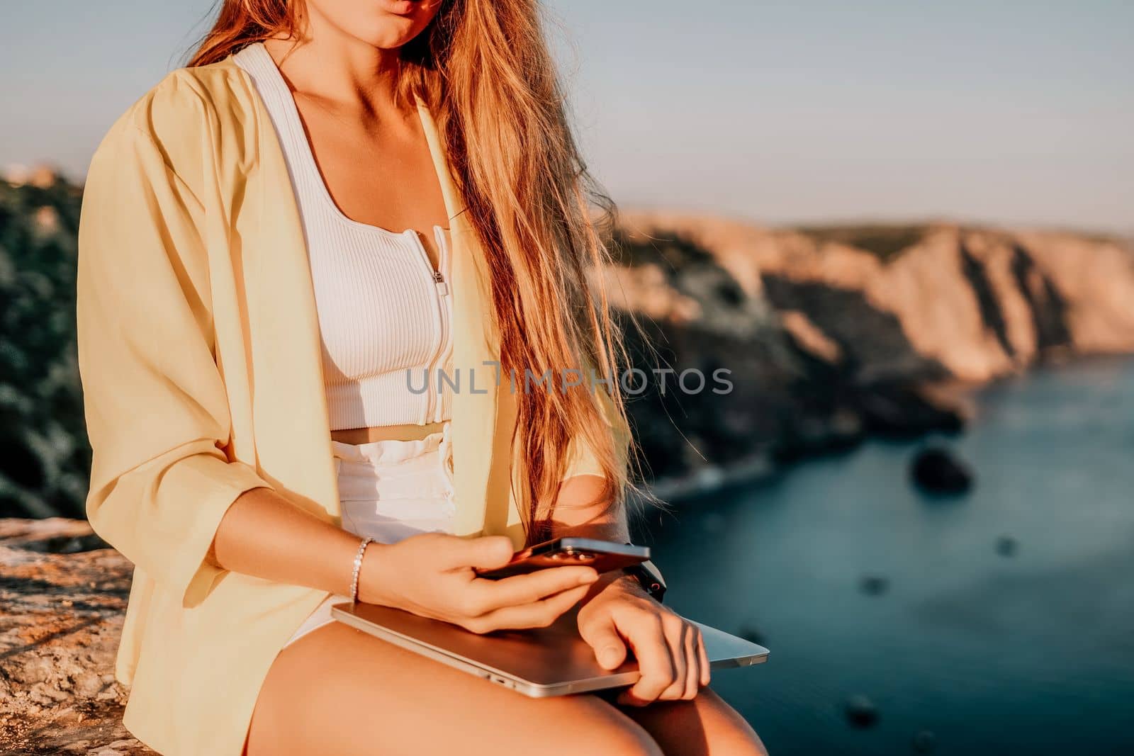 Digital nomad, Business woman working on laptop by the sea. Pretty lady typing on computer by the sea at sunset, makes a business transaction online from a distance. Freelance, remote work on vacation by panophotograph