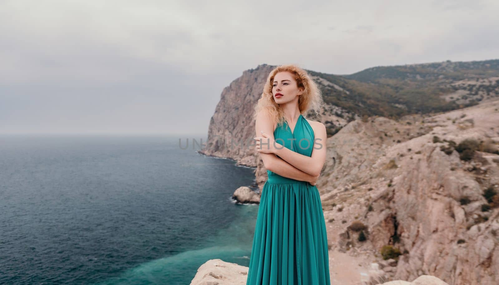 Redhead woman portrait. Curly redhead young caucasian woman with freckles looking at camera and smiling. Close up portrait cute woman in a mint long dress posing on a volcanic rock high above the sea by panophotograph