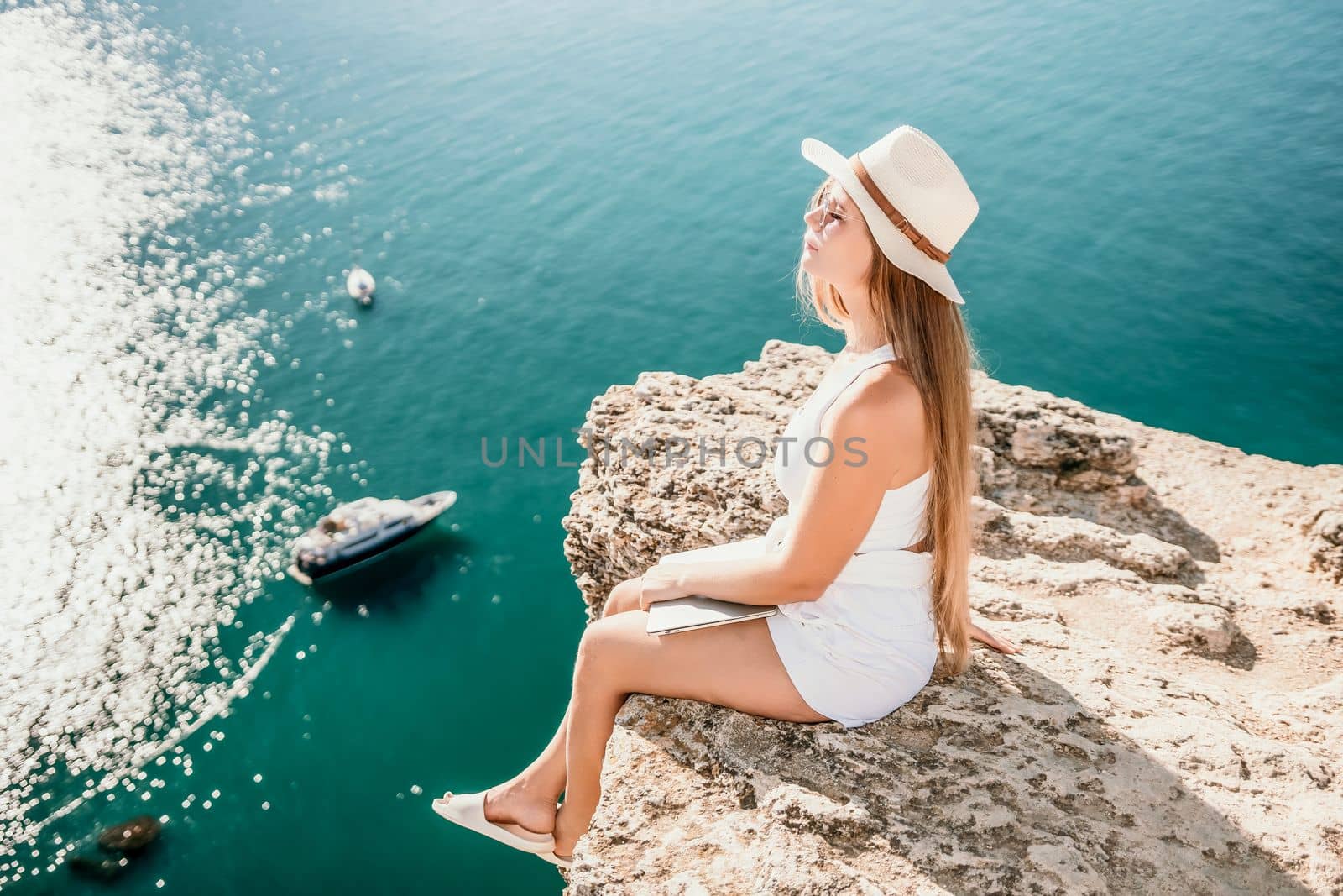 Digital nomad, Business woman working on laptop by the sea. Pretty lady typing on computer by the sea at sunset, makes a business transaction online from a distance. Freelance, remote work on vacation by panophotograph