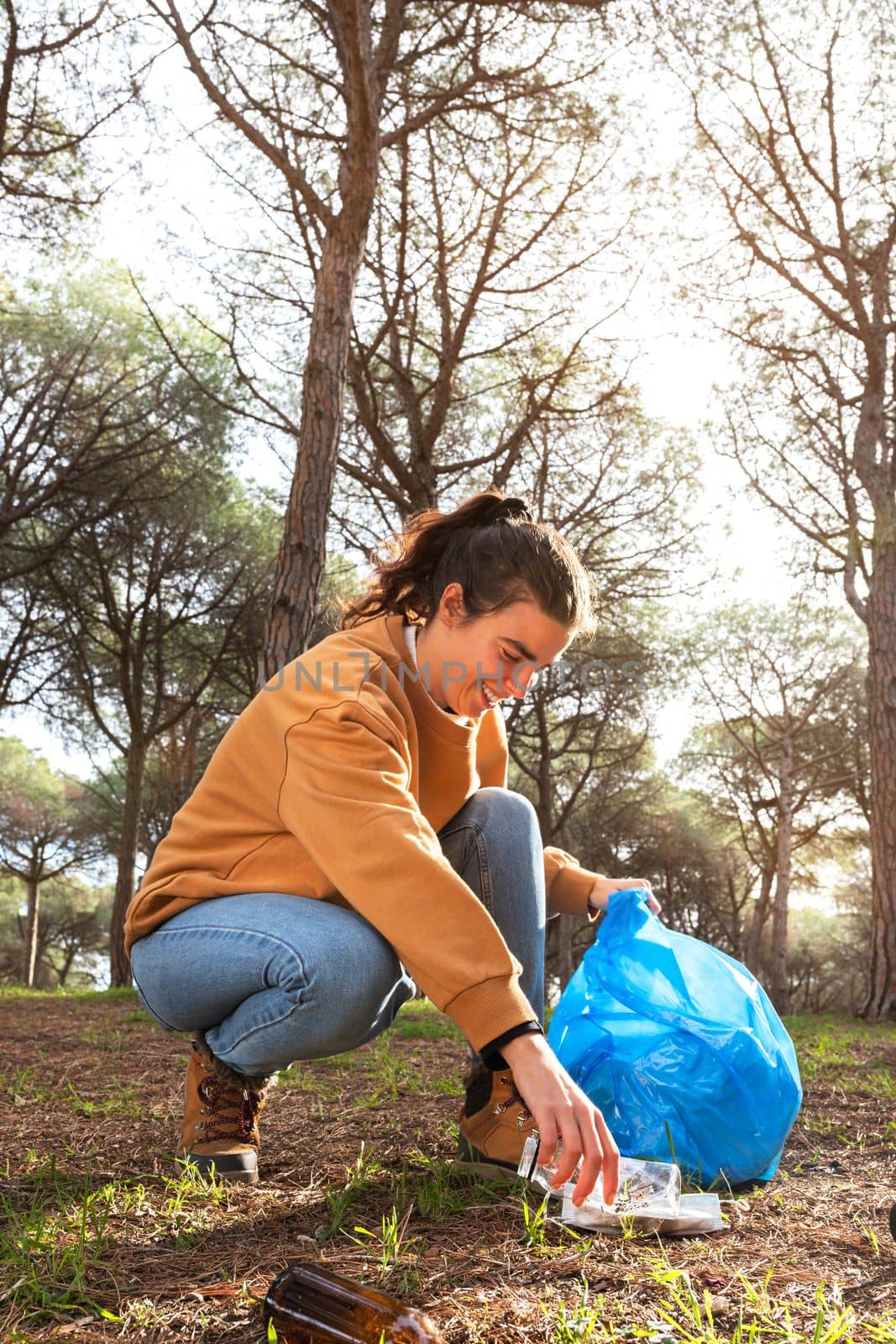 Happy young caucasian woman activist pick up plastic trash to clean forest. Copy space. Vertical image. by Hoverstock