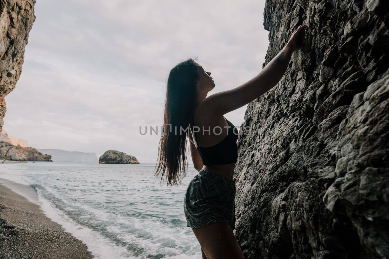 A girl climbs a rock. The athlete trains in nature. Woman overcomes difficult climbing route. Extreme hobby. Tourist woman rock climber hiking on mountains rocks over beautiful sea coast