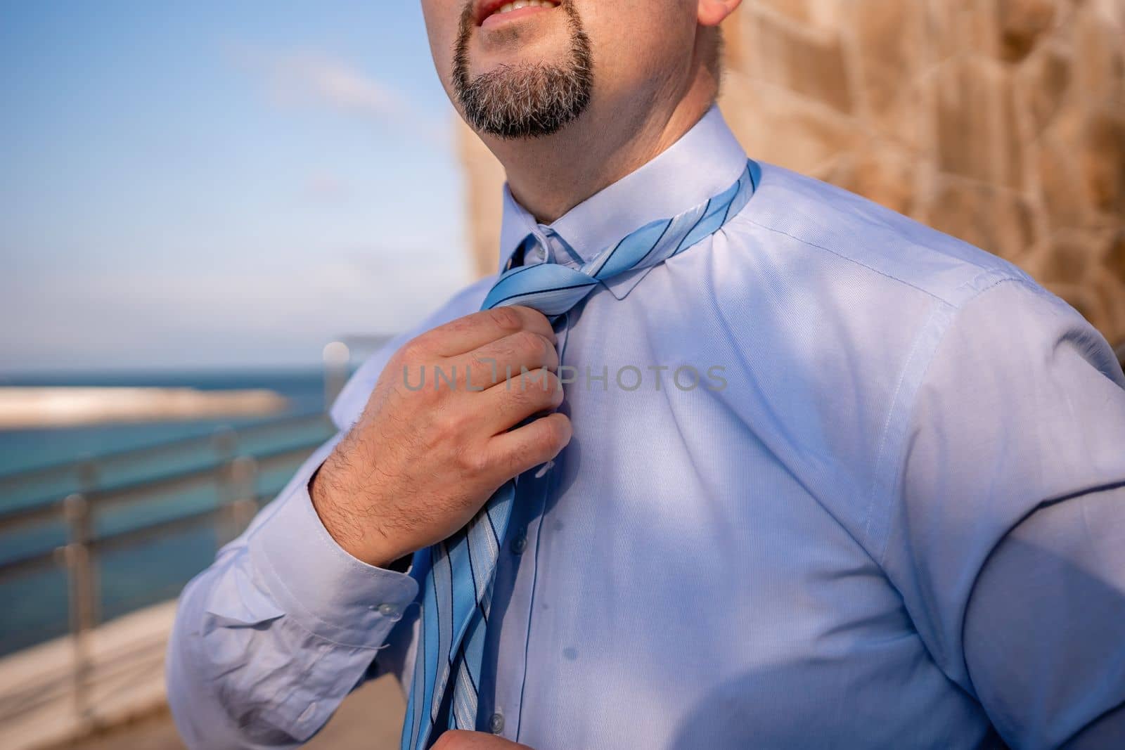 Close up of Man Adjusting Tie of Suit. Businessman in blue shirt straightens his tie, close-up by panophotograph