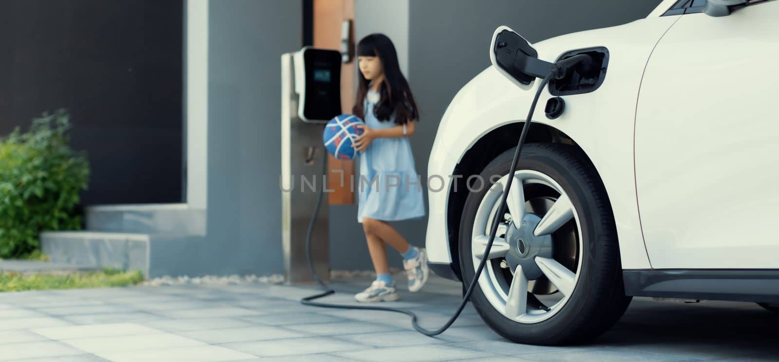 A playful and happy girl playing around at her home charging station providing a sustainable power source for electric vehicles. Alternative energy for progressive lifestyle.