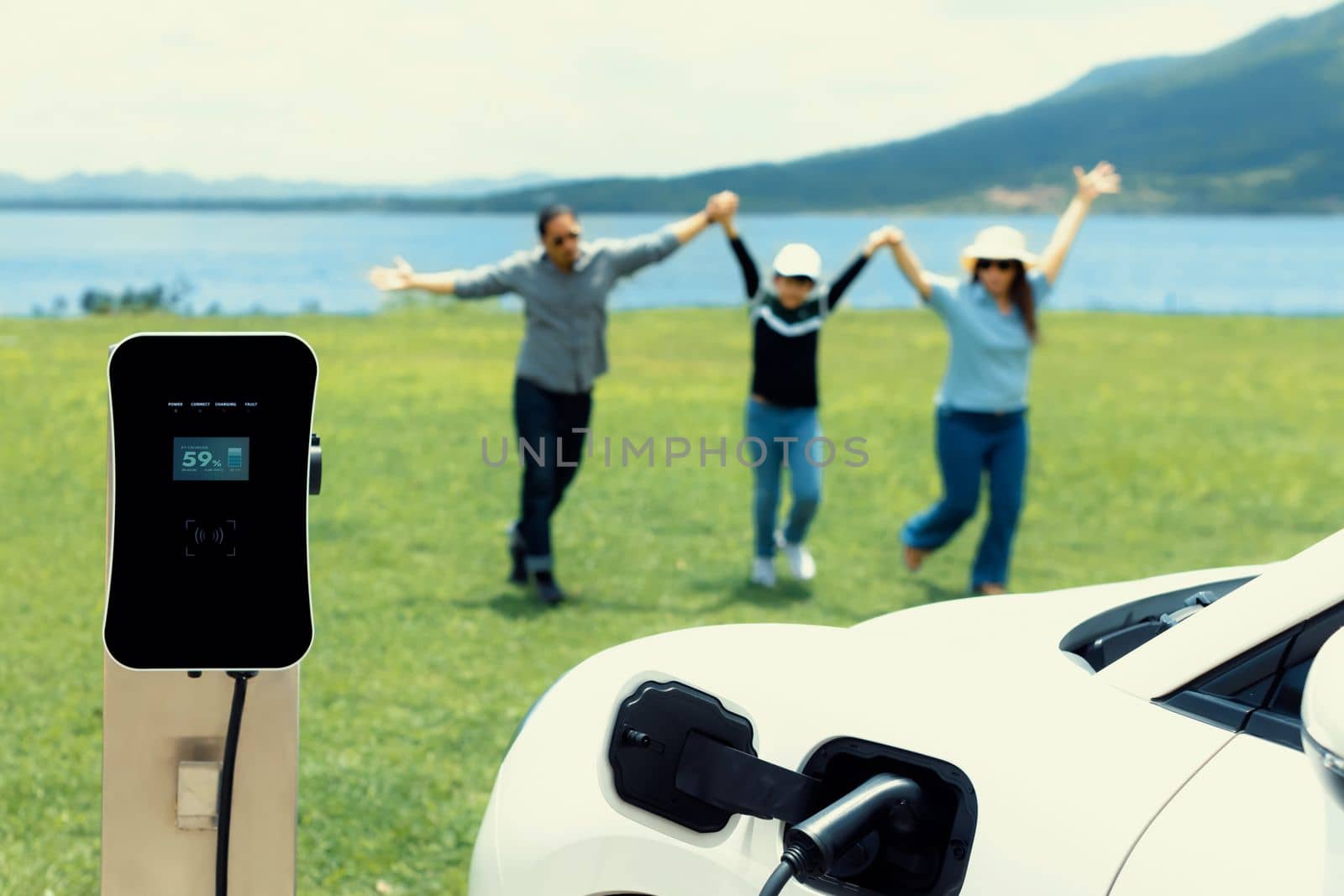 Concept of progressive happy family enjoying their time at green field and lake with electric vehicle. Electric vehicle driven by clean renewable from eco-friendly power sauce.