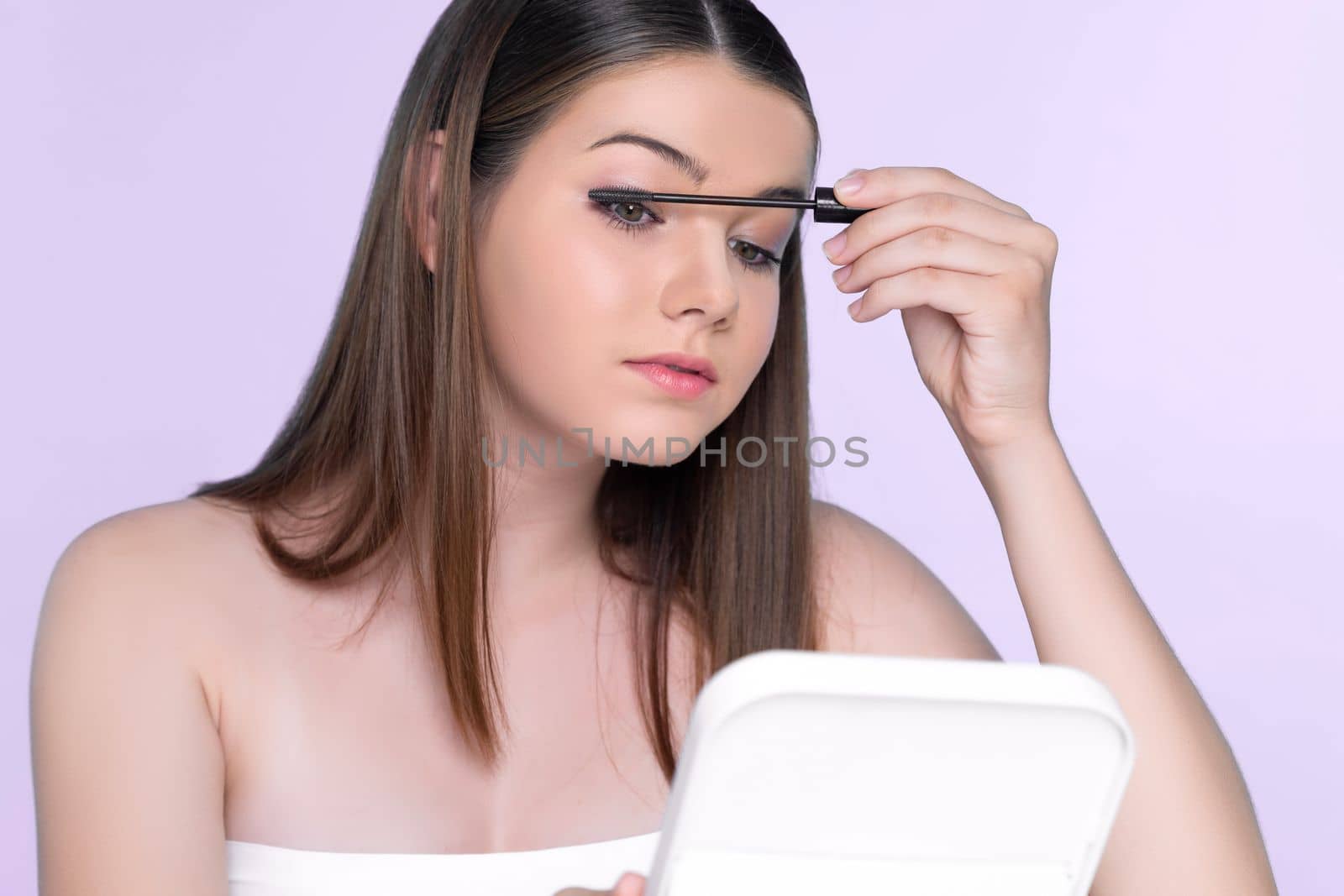 Closeup portrait of young charming applying makeup eyeshadow on her face with brush, mascara with flawless smooth skin for beauty concept.