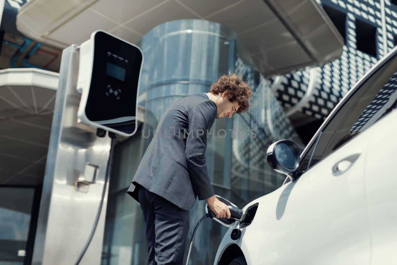 Below view closeup progressive black suit businessman recharge battery of EV car by biancoblue