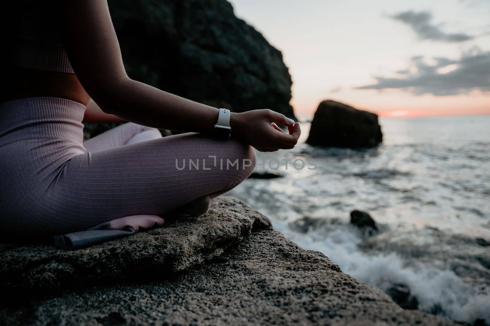 Young woman with black hair, fitness instructor in pink leggings and tops doing stretching and pilates on volcanic rocks near the sea on sunset. Female fitness yoga routine concept. Healthy lifestyle. by panophotograph