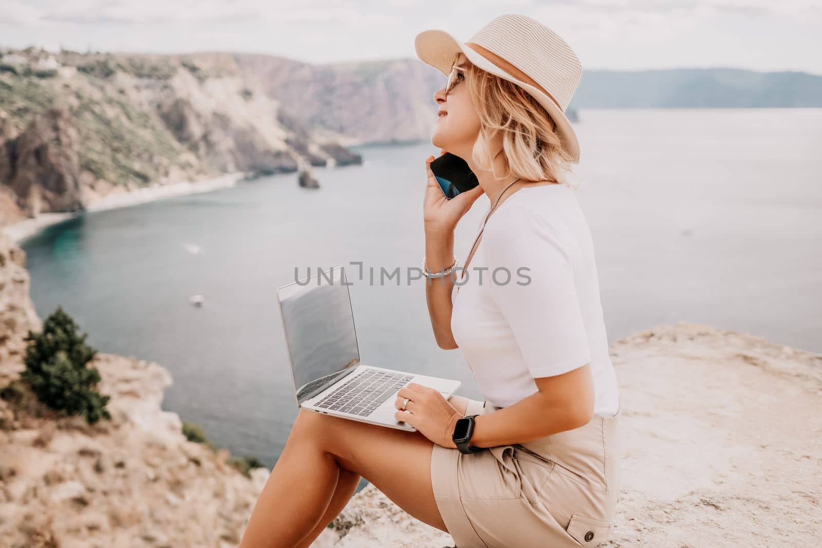 Digital nomad, Business woman working on laptop by the sea. Pretty lady typing on computer by the sea at sunset, makes a business transaction online from a distance. Freelance, remote work on vacation by panophotograph