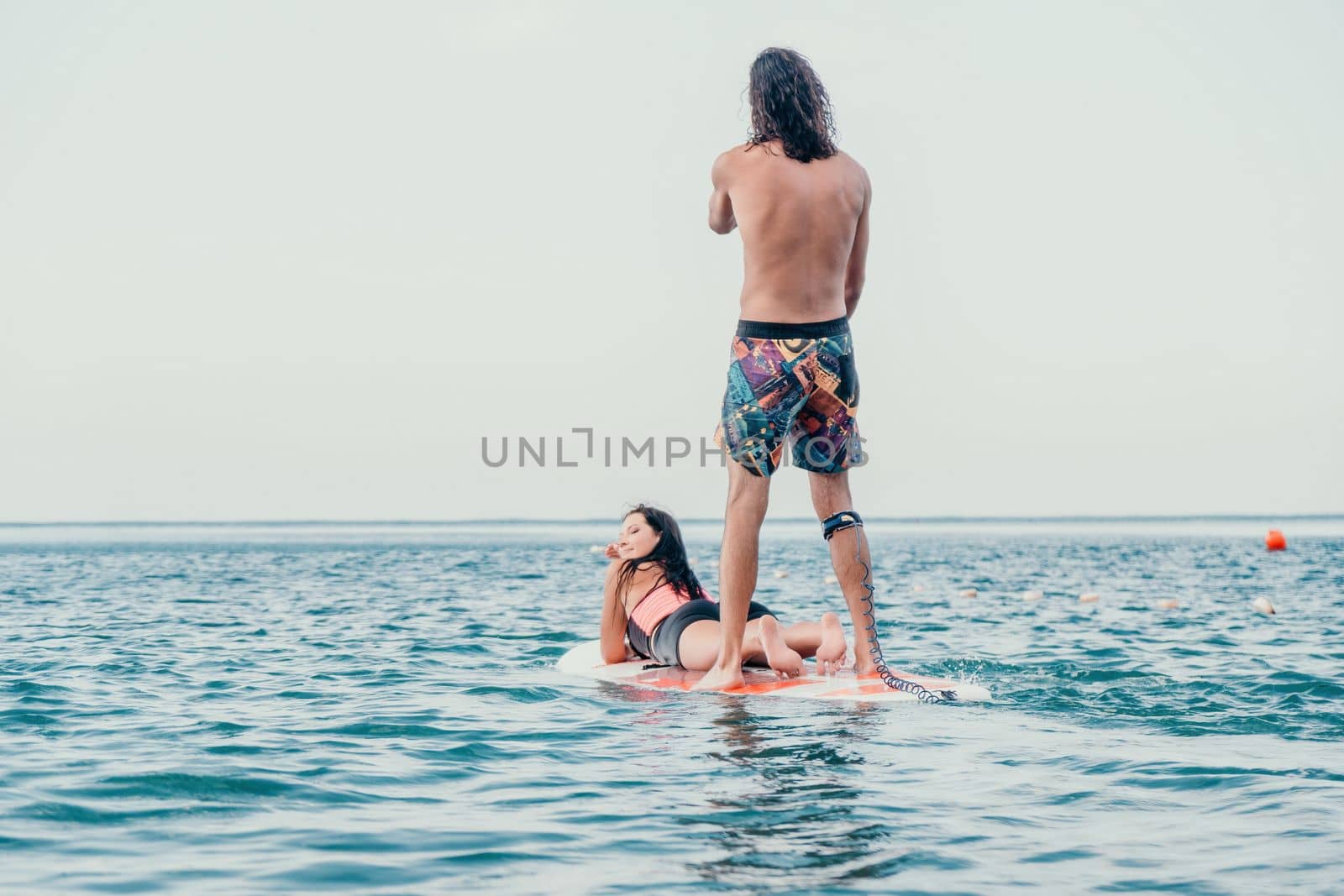 Sea woman and man on sup. Silhouette of happy young woman and man, surfing on SUP board, confident paddling through water surface. Idyllic sunset. Active lifestyle at sea or river