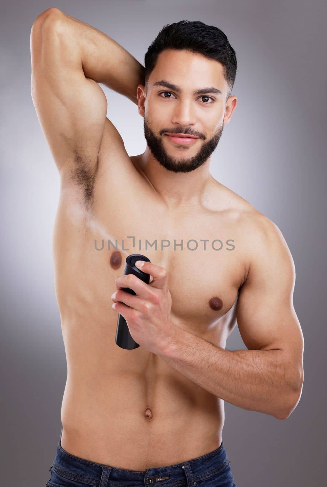 Keeping myself fresh and dry. a man spraying deodorant into his armpits against a studio background. by YuriArcurs