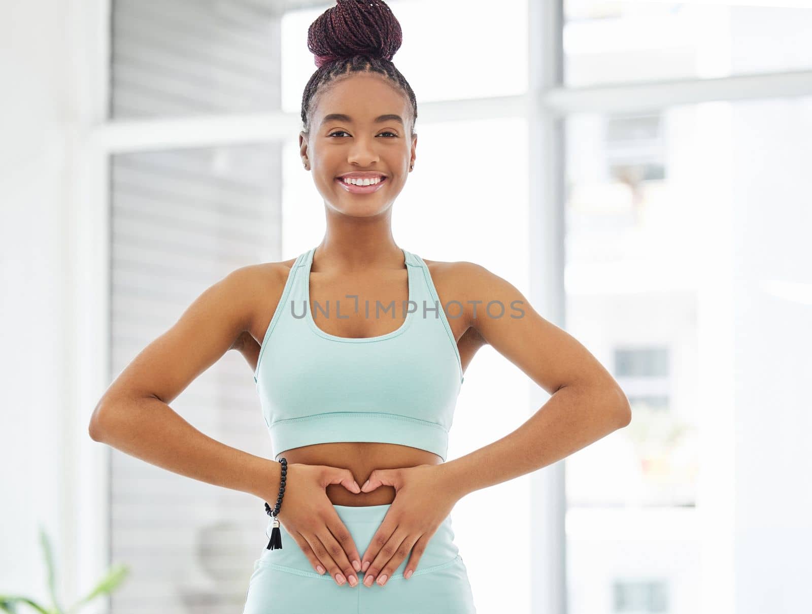 Yoga is good for your gut. a young woman standing alone in the yoga studio and making a heart shaped gesture over her stomach