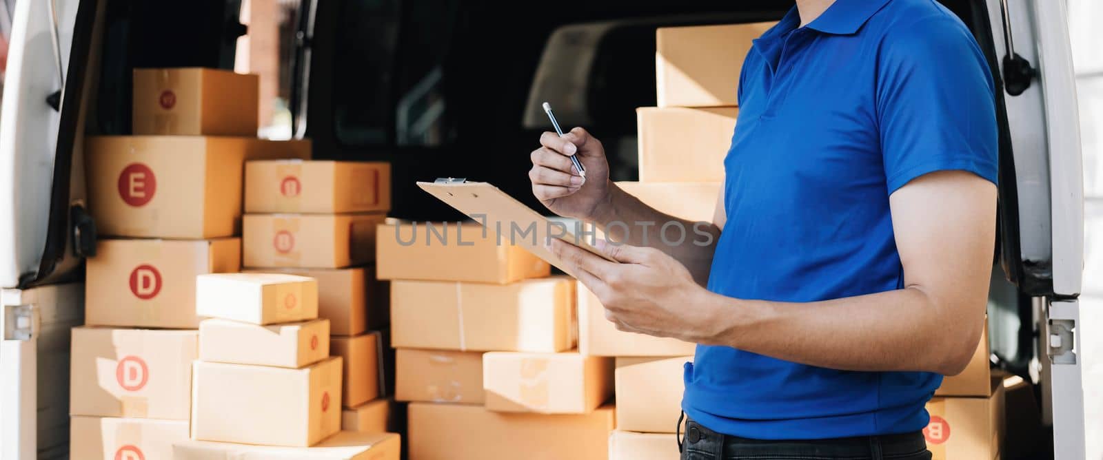 Closeup asian young delivery man courier in uniform hold documents clipboard and box checking list parcel post boxes near a car for service shipment to customer, Online shopping service concepts..