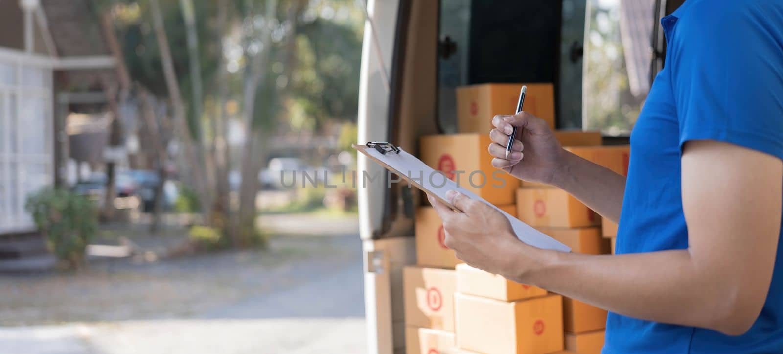 Closeup asian young delivery man courier in uniform hold documents clipboard and box checking list parcel post boxes near a car for service shipment to customer, Online shopping service concepts..