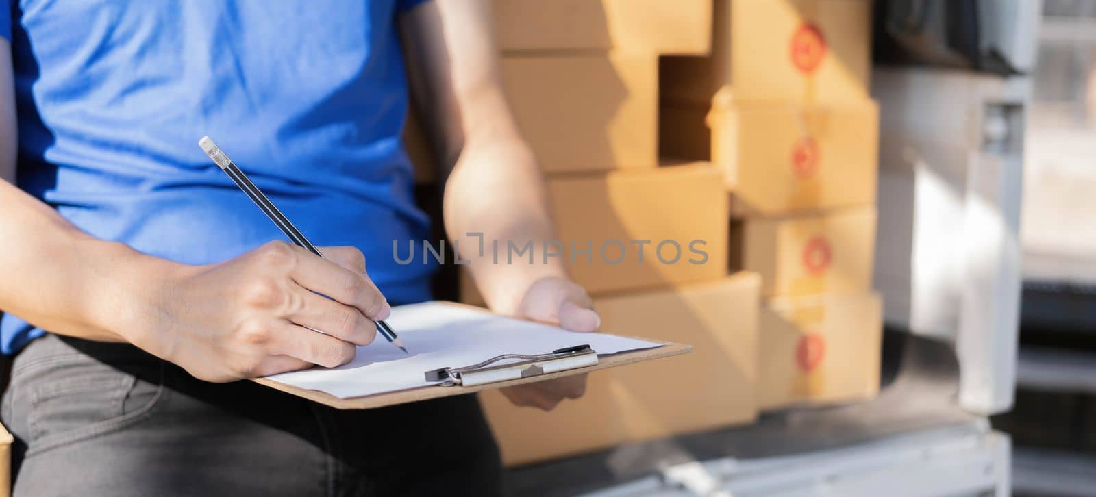 Closeup asian young delivery man courier in uniform hold documents clipboard and box checking list parcel post boxes near a car for service shipment to customer, Online shopping service concepts..