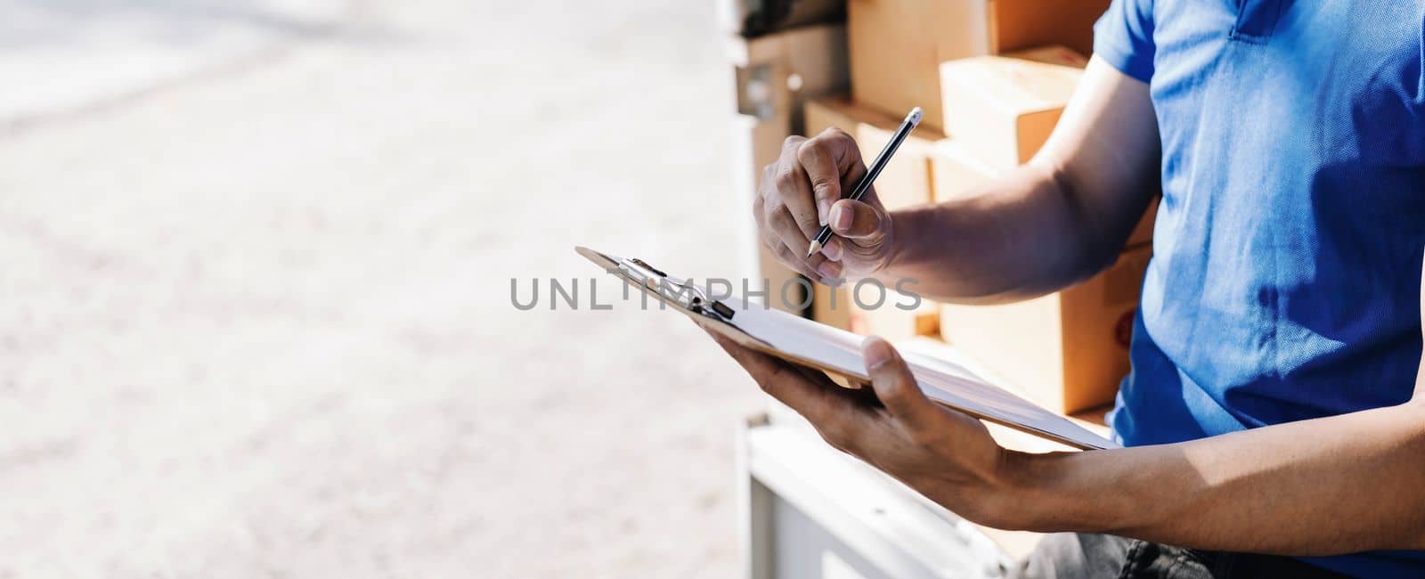 Closeup asian young delivery man courier in uniform hold documents clipboard and box checking list parcel post boxes near a car for service shipment to customer, Online shopping service concepts..