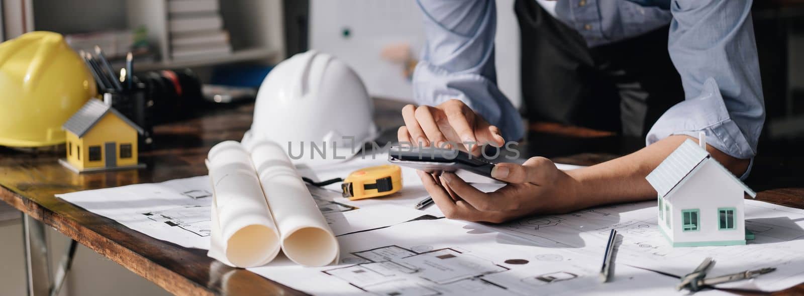 Image of engineer drawing a blue print design building or house, An engineer workplace with blueprints, pencil, protractor and safety helmet, Industry concept..