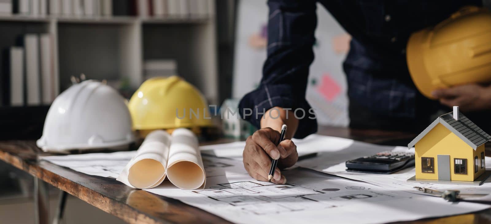 Image of engineer drawing a blue print design building or house, An engineer workplace with blueprints, pencil, protractor and safety helmet, Industry concept..