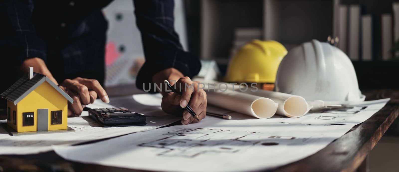 Image of engineer drawing a blue print design building or house, An engineer workplace with blueprints, pencil, protractor and safety helmet, Industry concept by wichayada