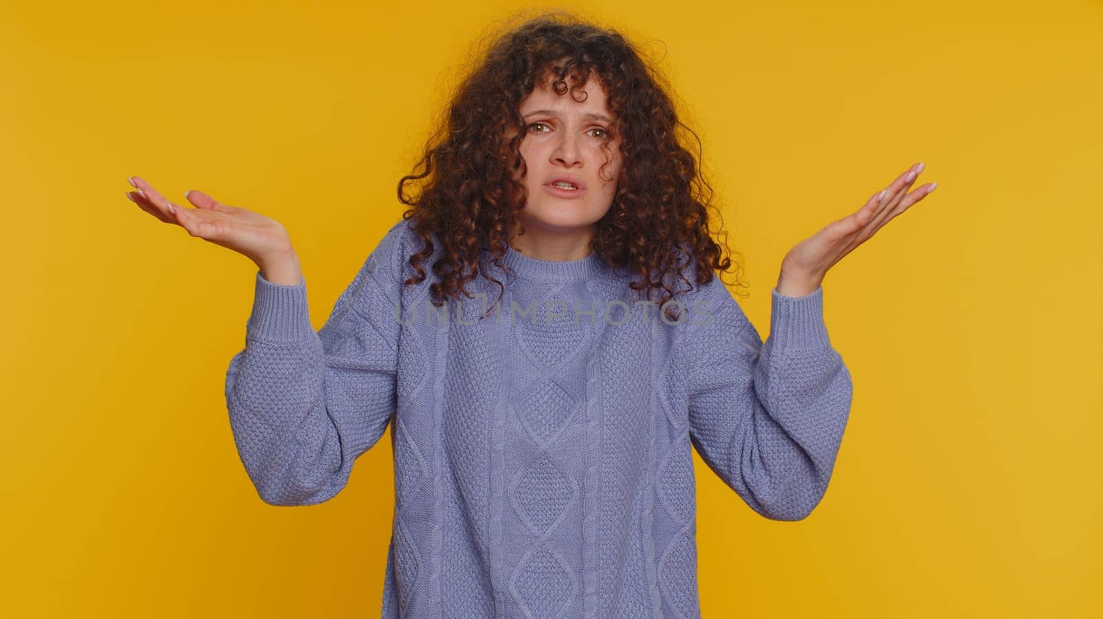 What Why. Sincere irritated woman raising hands in indignant expression asking reason of failure demonstrating disbelief irritation by trouble. Confused curly haired girl isolated on yellow background