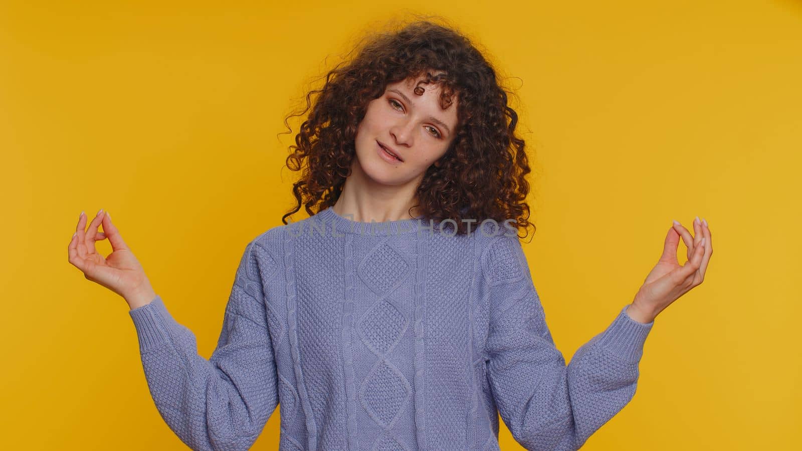 Keep calm down, relax, inner balance. Curly haired woman breathes deeply with mudra gesture, eyes closed, meditating with concentrated thoughts, peaceful mind. Young girl on yellow studio background
