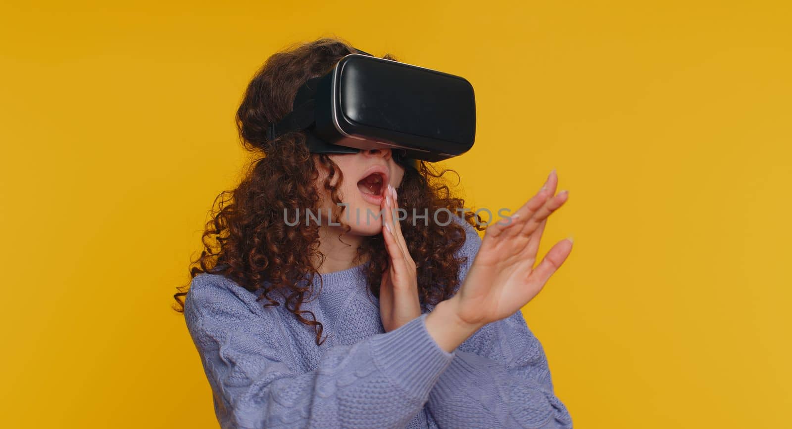 Young woman using headset helmet to play simulation game app online. Watching virtual reality 3D 360 video content. Girl in VR goggles isolated on studio yellow background. Futuristic technology