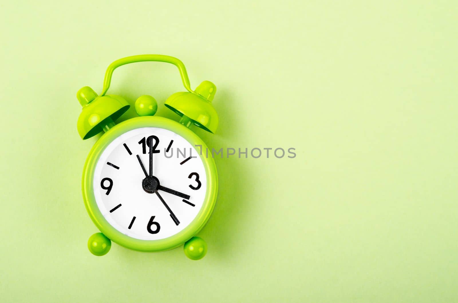 Green alarm clock on green colour background.