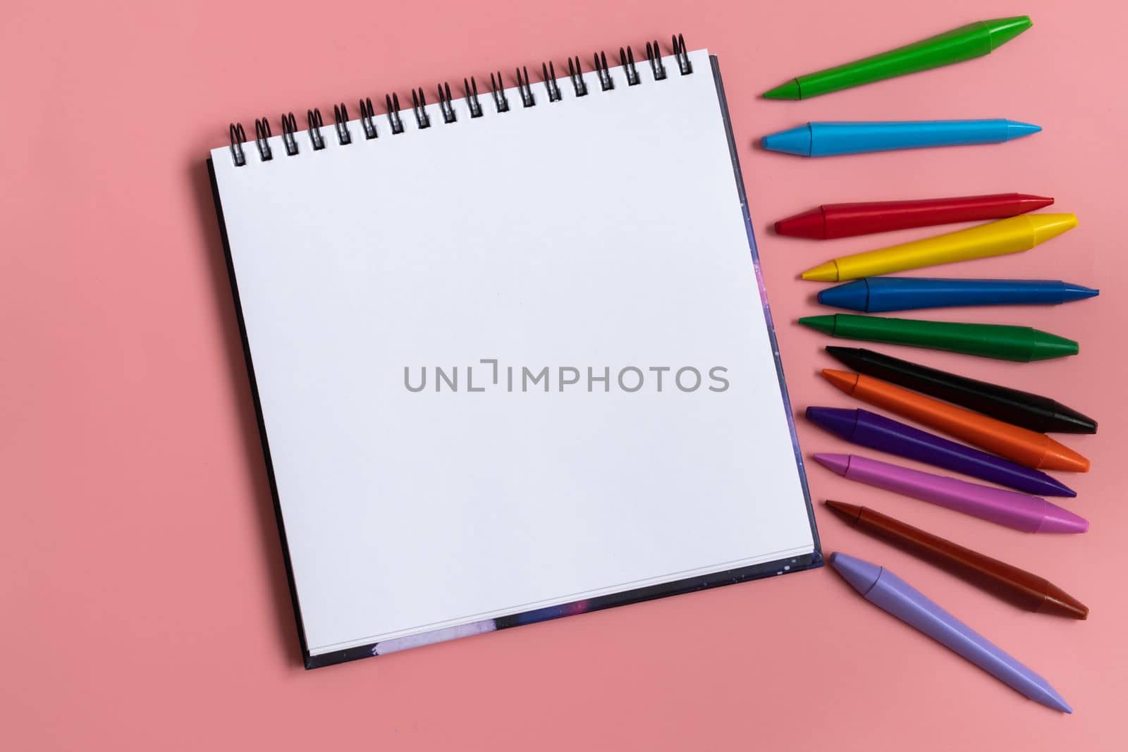 Open sketchbook with white empty blank. Colorful wax crayons on the pastel pink background. Flat lay composition. by Ri6ka