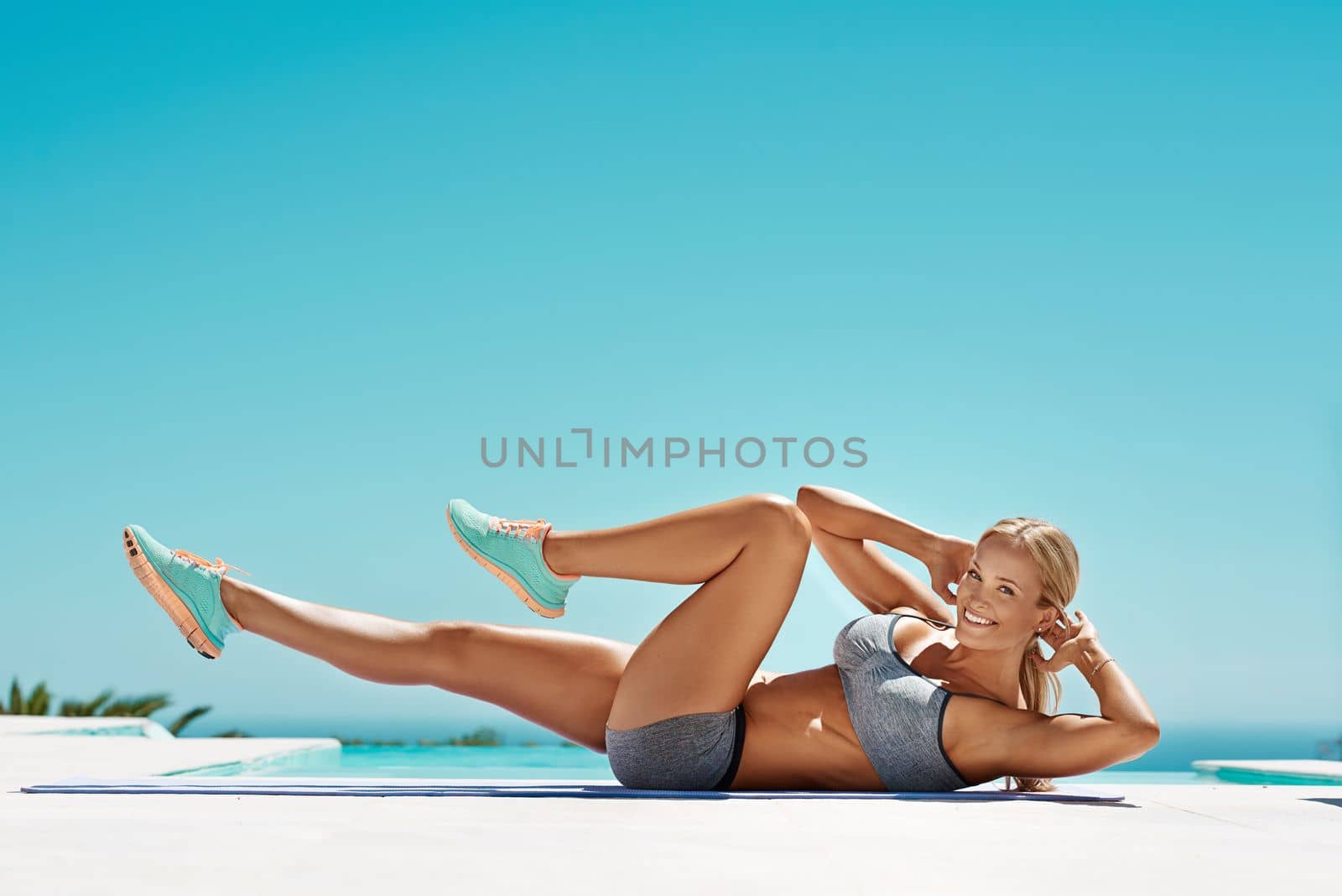 Fitness is true happiness. an attractive young fit woman in workout clothes exercising by the pool on a sunny day. by YuriArcurs