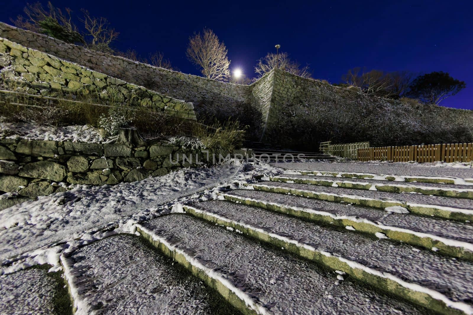 Snow covered steps to historic stone castle wall on cold winter night by Osaze