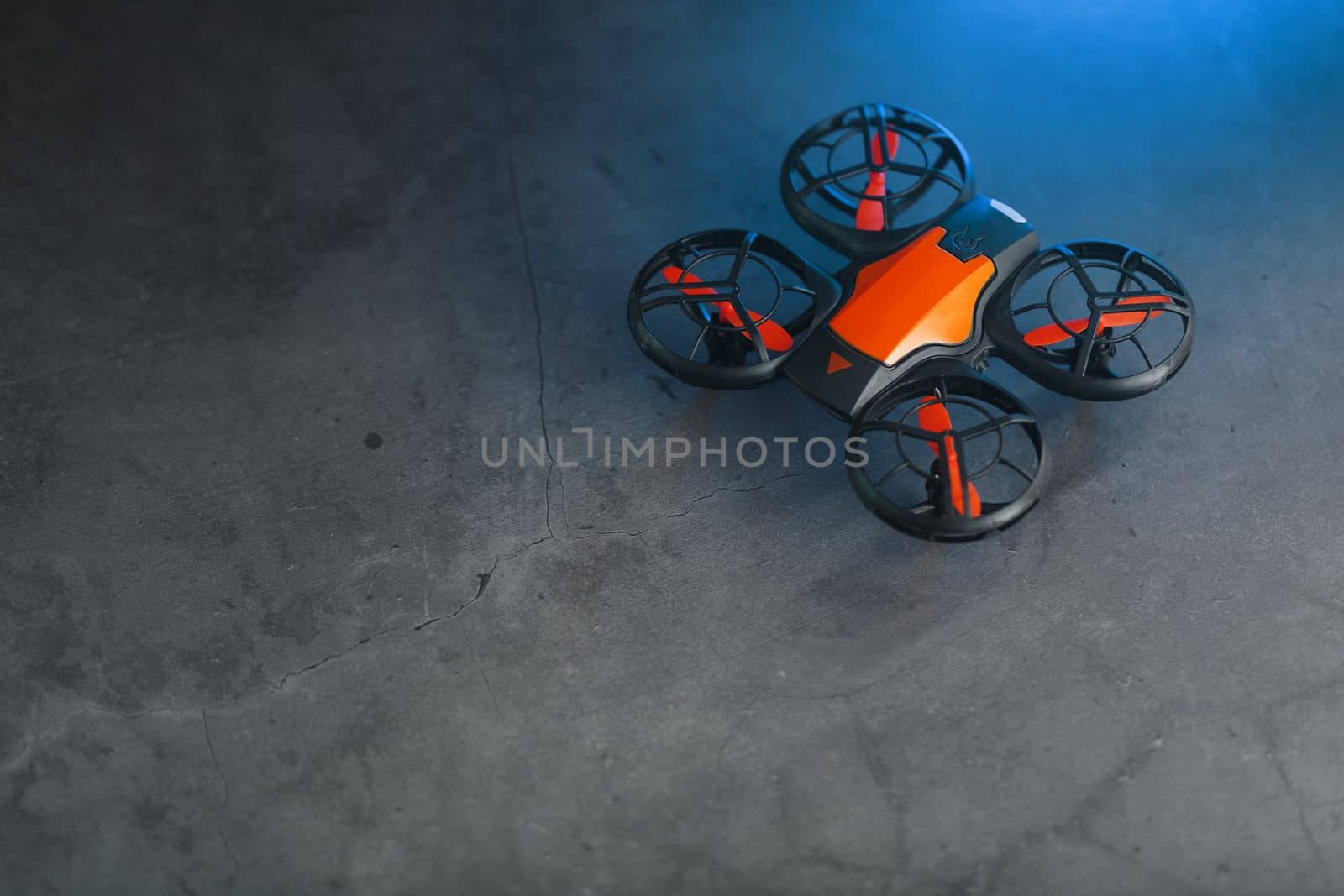 Orange quadcopter mini spy drone on a dark background with blue backlight by AlexGrec