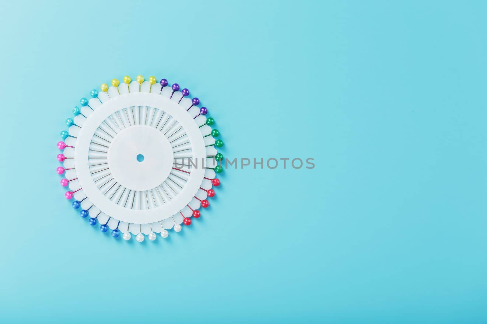 A set of multicolored needles pins in a round platform on a blue background with free space