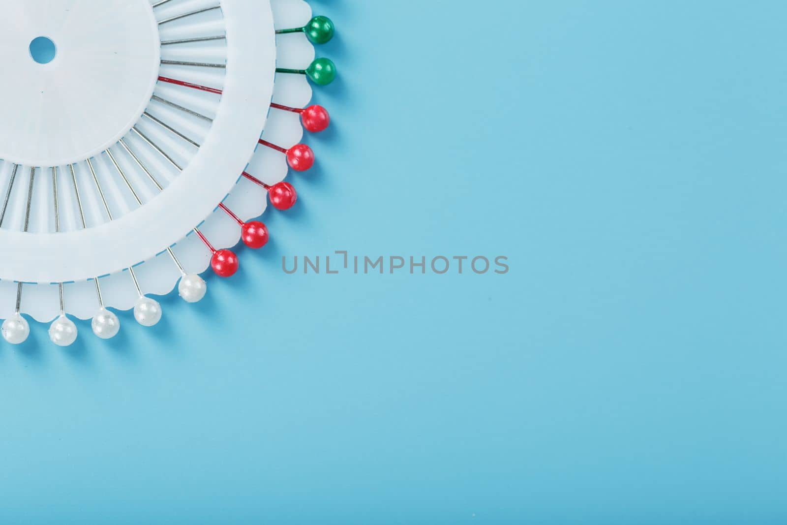 A set of multicolored needles pins in a round platform on a blue background with free space